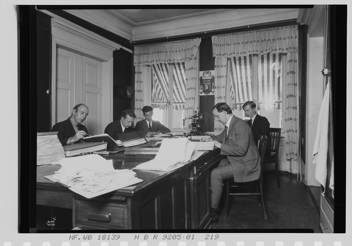 Fem menn sitter sammen på et kontor, Vinmonopolet. Fotografert 1924.