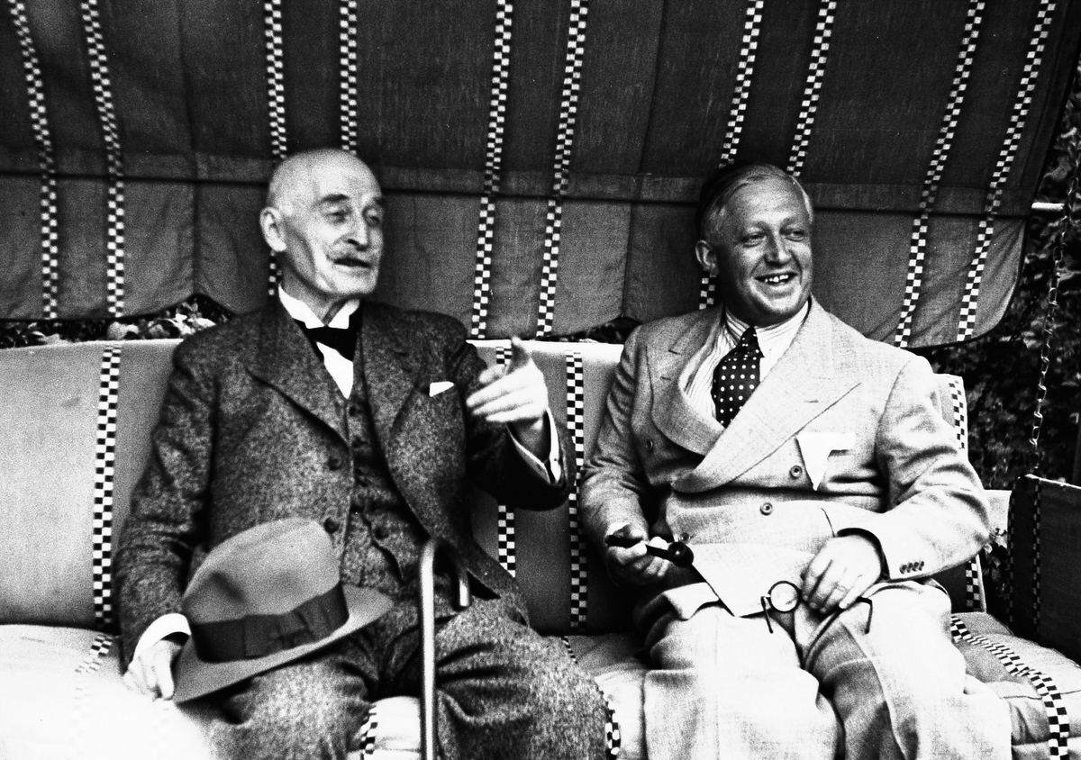 To kjente herrer, forfatter Knut Hamsun og forlagsdirektør Harald Grieg, nyter sommeren i hagen hos Grieg.
