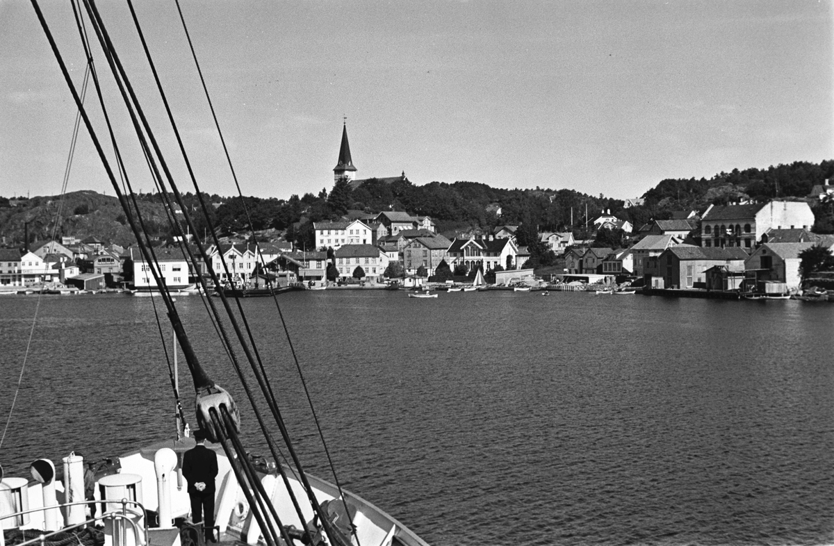 Innseilingen til Grimstad, hus langs sjøen og Grimstad kirke i bakgrunnen.