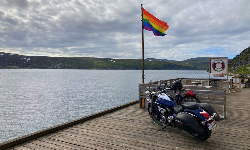 Kaia utenfor Foldalbruket i sollys, pride flagg og motorsykkel.