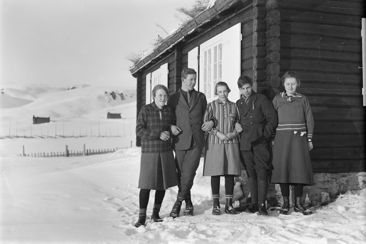 Øksendalen. Gruppe nr. 5 fra Gudbrandsdal Fylkesskole. Tre kvinner og to menn utenfor tømmerhytte med torvtak. Vinter.