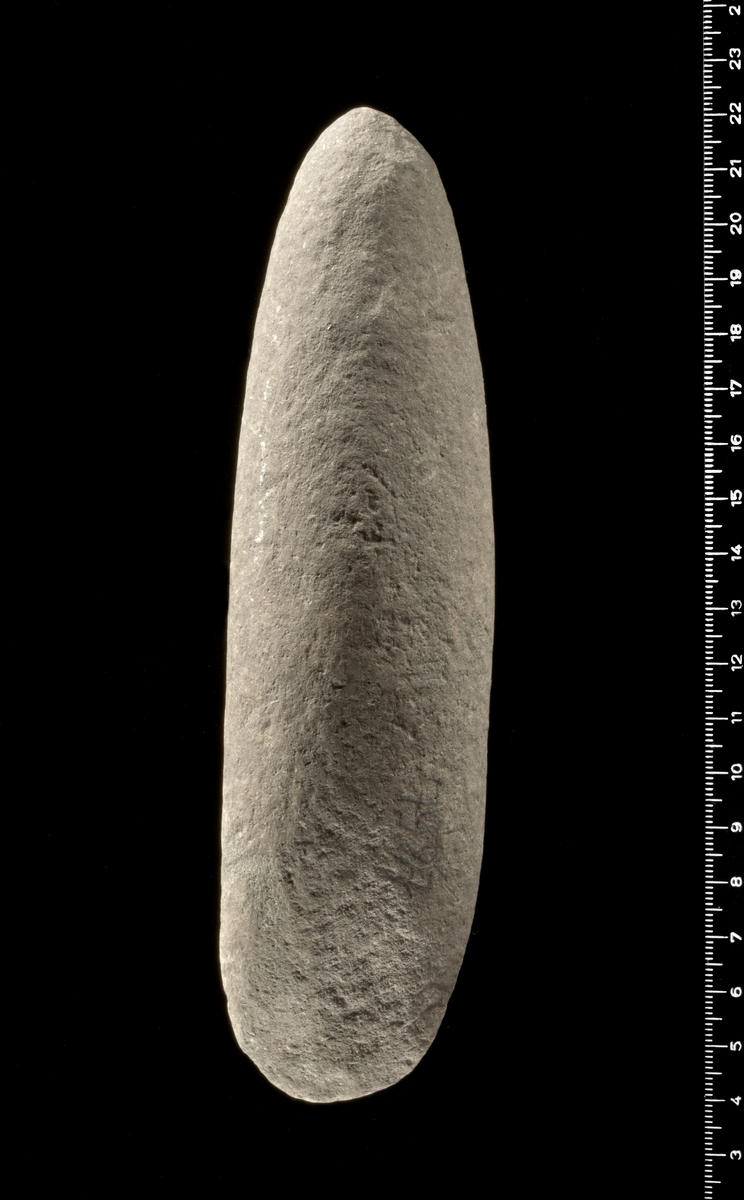 Kile af Sten af ovalt Tversnit med tilspidset Bane, temmelig tyk; har nu intet Spor til Slibning, der dog kan være udslettet ved Forvitring. 18 cm. lang, 3,8 cm. bred i Eggen.7987.
