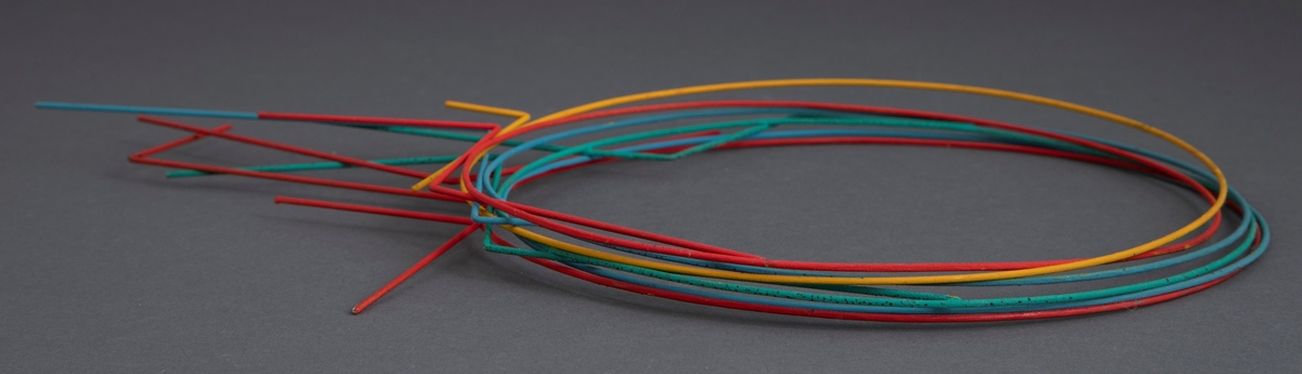 Halssmykke bestående av seks separate ringer av stål som hver har en påloddet dekorasjon sammensatt av rette tråder av stål. Alt er dekket av neopren i ulike farger. To ringer er røde, to blå, en gul og en grønn.