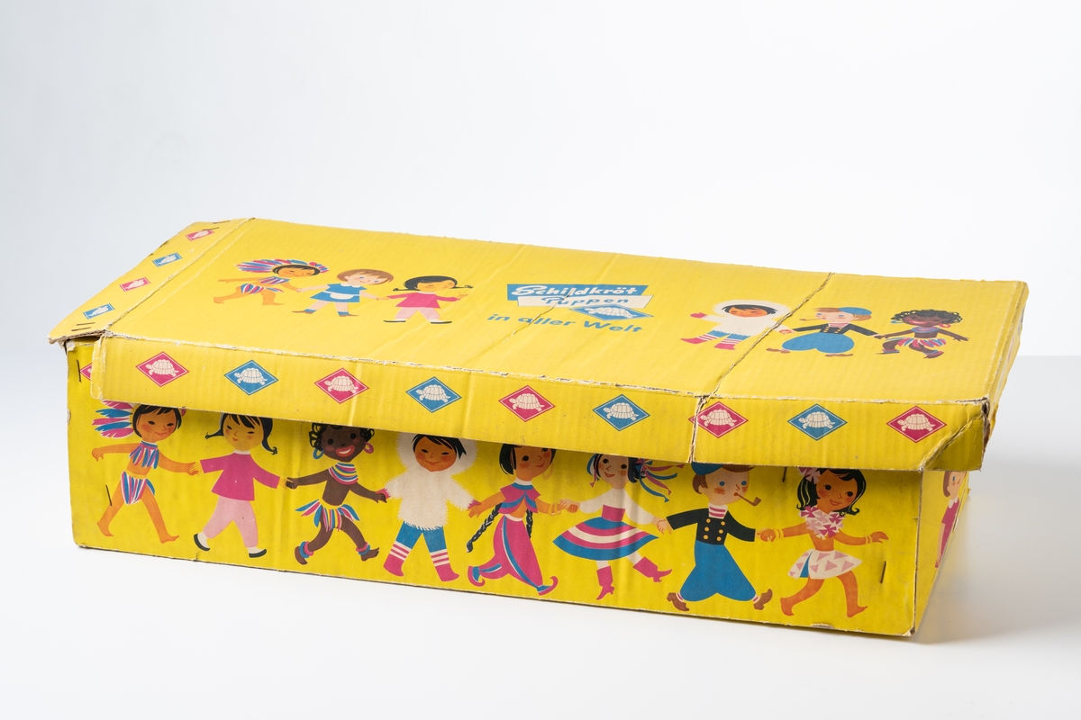 Originalkartong, låda med lock, till en så kallad Sköldpaddsdocka, JM.56864:1. Dockan är av märket Schildkröt Puppen, tillverkad av Schildkröt-Puppen, före detta Rheinische Gummi- und Celluloidfabrik, Tyskland. Vaumärket är en sköldpadda. 

Förpackning av gulfärgad wellpapp med tryckta illustrationer i flera färger i form av barnfigurer från hela världen. Lådans öppning har en vågig kant. På lådan tryckt text: ”Schildkröt Puppen 8706w/56 ’Mama’ 1 Stück Made in Western Germany”, och ”Tortoise Dolls all over the word”, "Tortue Poupées dans tout le monde”. På locket tryckt text: “Schildkröt Puppen in aller Welt”. Kartongen har skador.

Se vidare Historik.