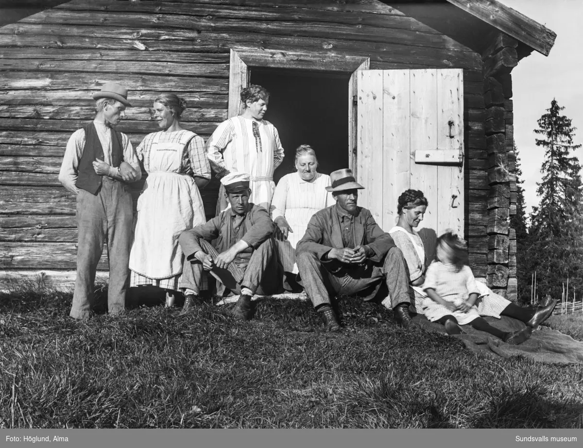 Gruppbild vid ingången till en fäbodstuga, sju vuxna och ett barn. Längst till vänster står Niklas Bergström. På bild nummer två sitter en av kvinnorna ensam i dörröppningen och utanför står smörkärna, ostformar och laggkärl.