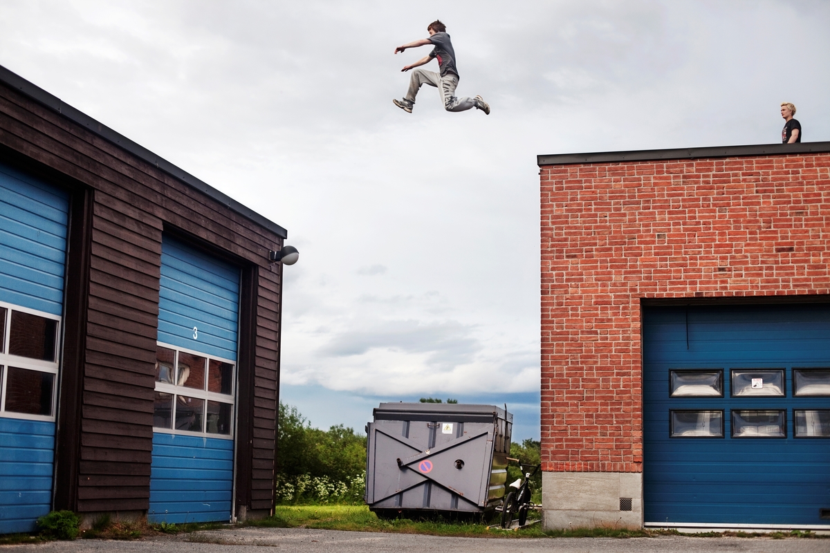 En gutt hopper mellom to hustak, han er fotografert midt i svevet. Fra serien "Everybody Knows This is Nowhere".