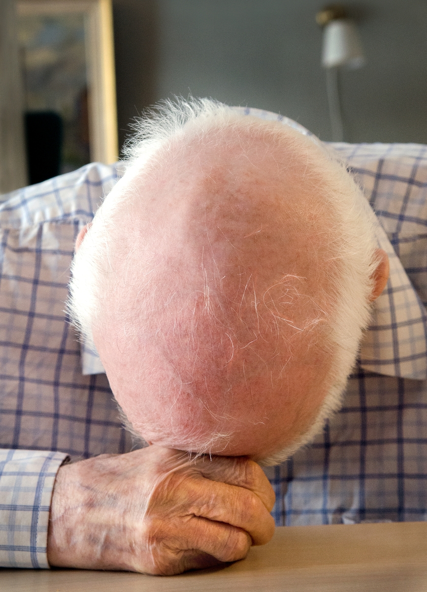 En gammel mann hviler hodet mot bordet. Fotografiet er en del av serien Isolasjon fra skjermet avdeling for demente på et sykehjem i Oslo.
