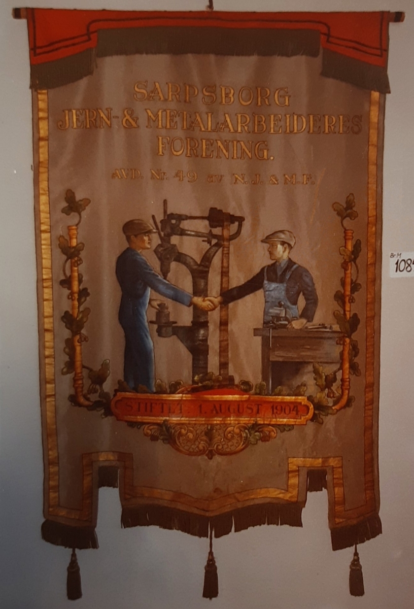 Tekst, to menn i håndtrykk, bormaskin, border (forside) krans og redskaper (bakside)