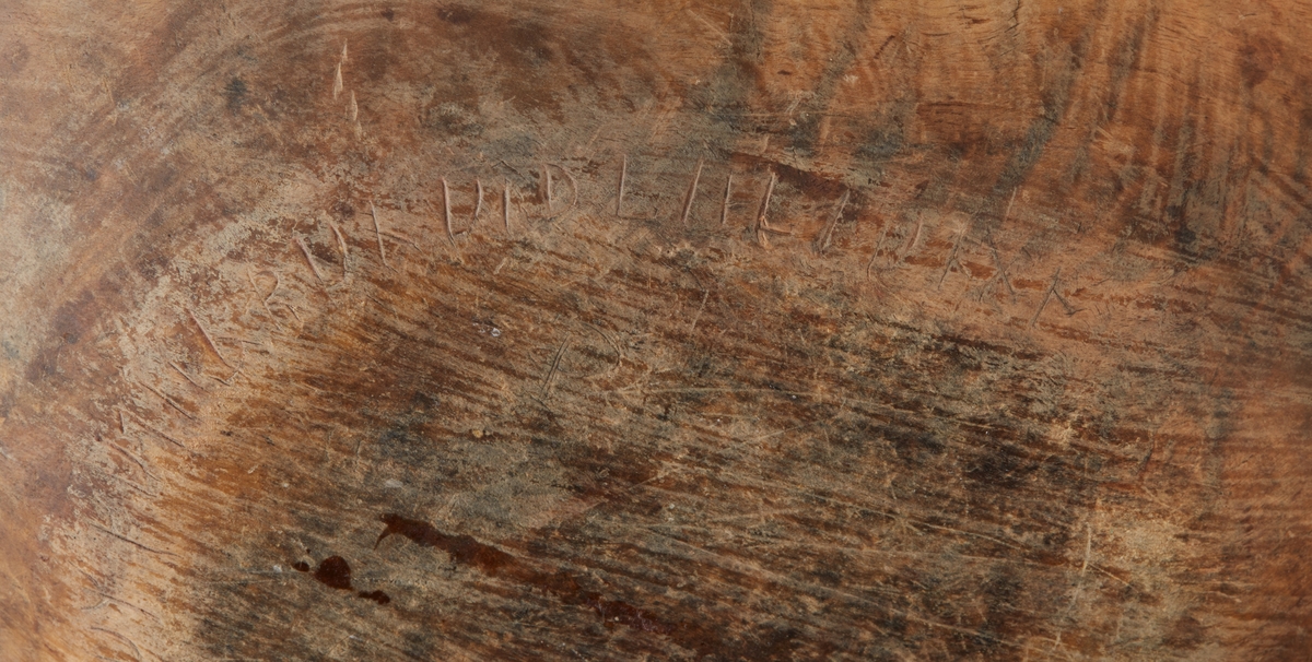 Skål av trä. En stor spricka i ena kortsidan lagad med mässingstråd. Runt botten inristade dalrunor, bla årtal: "1717".
Bilagor finns med en del tolkningar av runorna.
