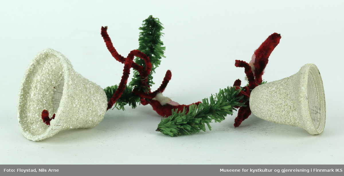 To juleklokker/ bjeller en liten og en stor med dekor av nisser og kunstige grangrener. Hver bjelle har dekor av kunstige grangrener og mørkerøde piperensere med et pålimt ansikt av en nisse. Nissene har hvite øyenbryn og blå øyne, med hvit bart og bomullsskjegg. Selve juleklokkene/ bjellene er laget av pappmasjé og er malt hvite, og dekorert med grovkornet glitter som gir bjellene en ruglete overflate.
