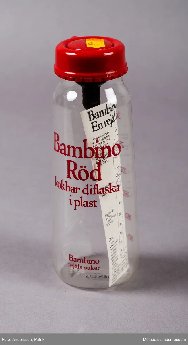 En genomskinlig plastflaska för matning av spädbarn. Flaskan har ett rött lock med napp funktion för matning. På flaskan finns en röd text med varumärket Bambino Röd. Flaskan ser oanvänd ut. Den har en orange extra pris lapp på locket. Den är ursprungligen inköpt på ICA och har kostat 15.60. Inuti flaskan finns en bruksanvisning. Flaskan är från 1981.
Bambino har tillverkat nappflaskor sedan 1950-talet. De marknadsför sig som tillverkare med en smart, funktionell och färgglad design för babytillbehör. Deras kärnvärden är enkelhet, funktion och glädje i vardagen.