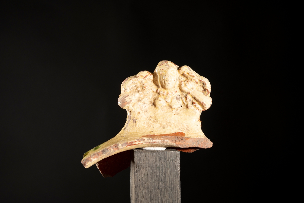Motivet med den tvestjärtade sjörjungfrun, även kallad melusine, är pressat in i leran med en stämpel. Handtagets ytterform följer sjöjungfruns former som är symetriska med de två fiskstjärtarna mot fästet mot skålen och jungfruns huvud mot ytterkanten av handtaget. Stilen är holländsk barock och de flesta fynd med denna dekor är daterade till 1660-tal.
