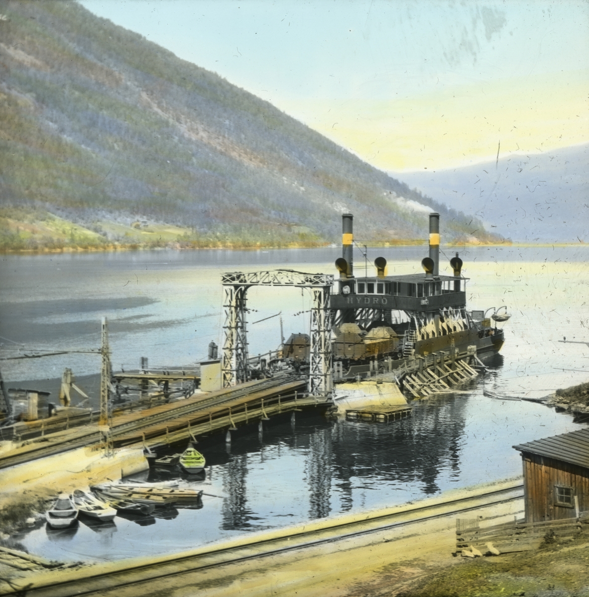Håndkolorert dias. Bilde av dampfergen Hydro liggende i havn ved Tinnosbanen på Tinnoset. Den fraktet jernbanevogner med hovedsakelig kunstgjødsel, ammoniumnitrat og ammoniakk, i tillegg til passasjerer.