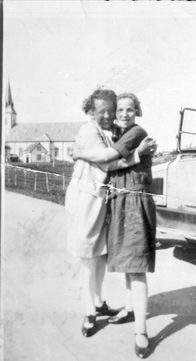 Amatørportrett av to kvinner stående ved en bil, Skånland kirke i bakgrunnen.