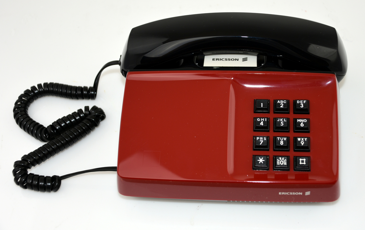 Telefonapparat, Diavox 'The Ericsson Royal 100', för export till USA, år 1984. För AT-system, huvudapparat, anknytningsapparat till abonnentväxel och sidoapparat. Bordsmodell med kåpa och mikrotelefon av svart plast, knappsats med 12 knappar för tonval, högohmig reglerbar ringklocka, elektretmikrofon och elektronisk talkrets med automatisk dämpningskompensering. I originalkartong med två extra apparathöljen i rött och vitt.
