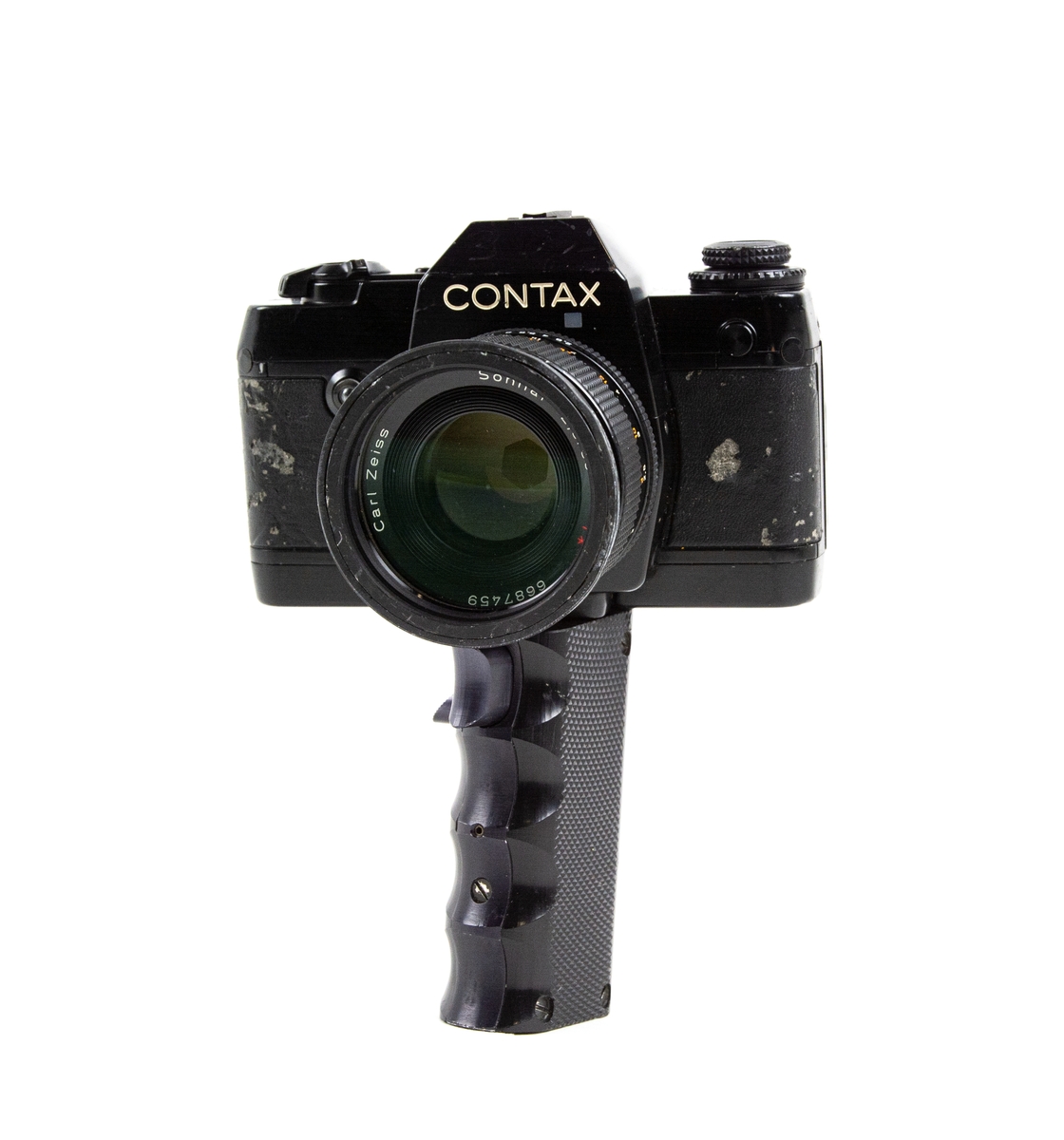 Handkamera HK 101 MT. På handkameran finns ett objektiv. Under kameran finns ett längre handtag varpå det finns 2 knappar för utlösning av film.
