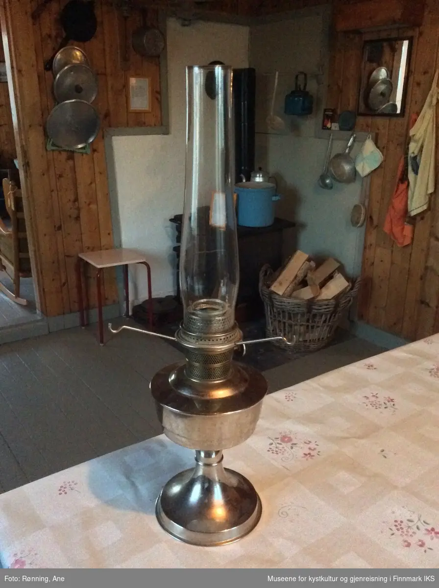 Lampen består av en rund lampefot i metall og har en beholder for flytende brennstoff. Opp på den er det plassert et sylindrisk glassrør som beskytter flammen når det er tent i lampen. Lampeskjermen er av lys, blomstret stoff som har et hull etter en brannskade.