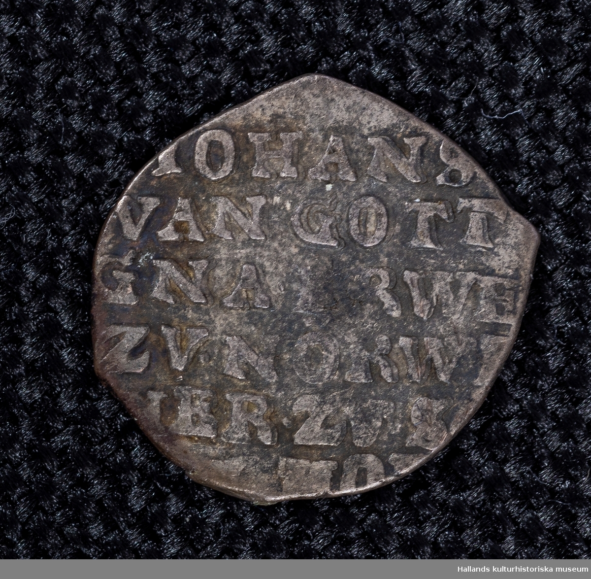 Arkeologiskt föremål. Holländskt silvermynt. Präglingsår 1675.På ena sidan överst präglingsåret. under sköld av en krona, omgiven av en strålkrans och två pilar. På ömse sidor bokstäverna "Z" och "L". På motstående sida följande text: "JOHANS VANGOTT GNA...RWE ZV. NORW  IER ZVS" Myntet är sönderklippt. 