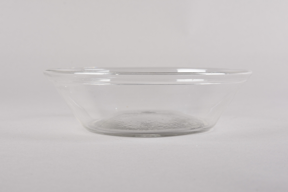 Rund glasskål med svakt kvelva botn, korpus har skrånande form opp mot munningsrand med fals. Puntmerke i botn.