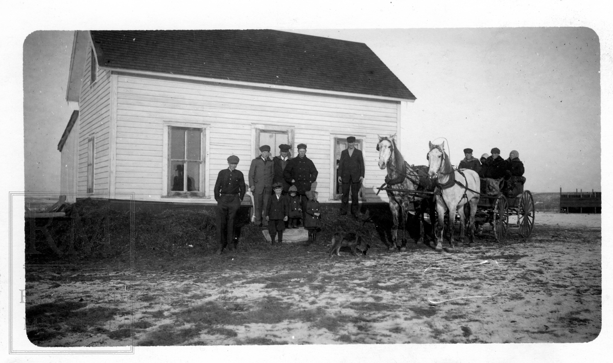 En gruppe samlet utenfor et hus. Fire sitter i en vogn med to hester i draget.