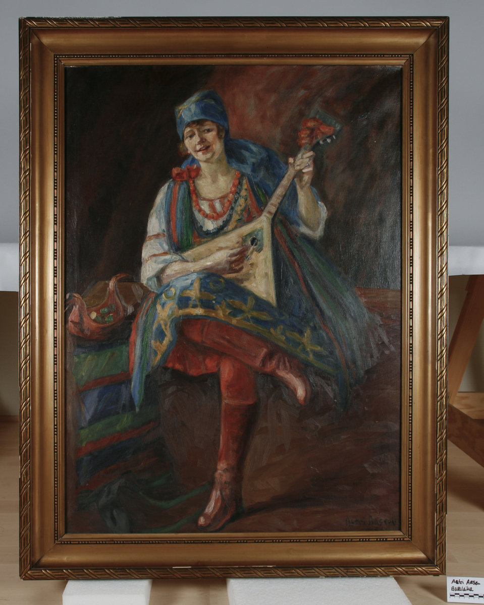 Victoria Bachke ikledd russisk folkedrakt. Hun spiller på et instrument, en balalaika(regnes som Russlands nasjonalinstrument). Ved hennes side en rød ølhøne.