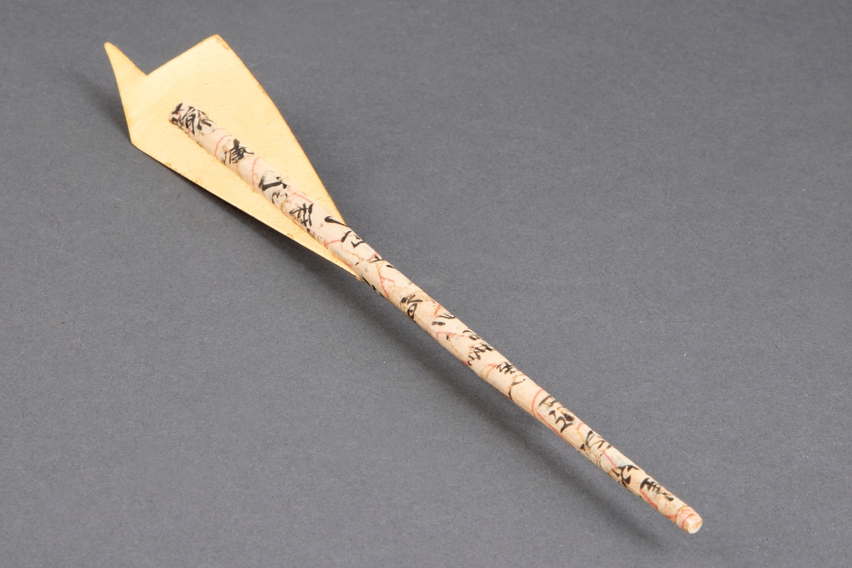 Brosje bestående av en spisepinne i bambus dekket med japansk papir med skrifttegn på. På den øvre delen er det festet en uregelmessig sølvplate med pålagt gullfolie. Denne platen en tilnærmet pilespissformet. Lang nål på baksiden.