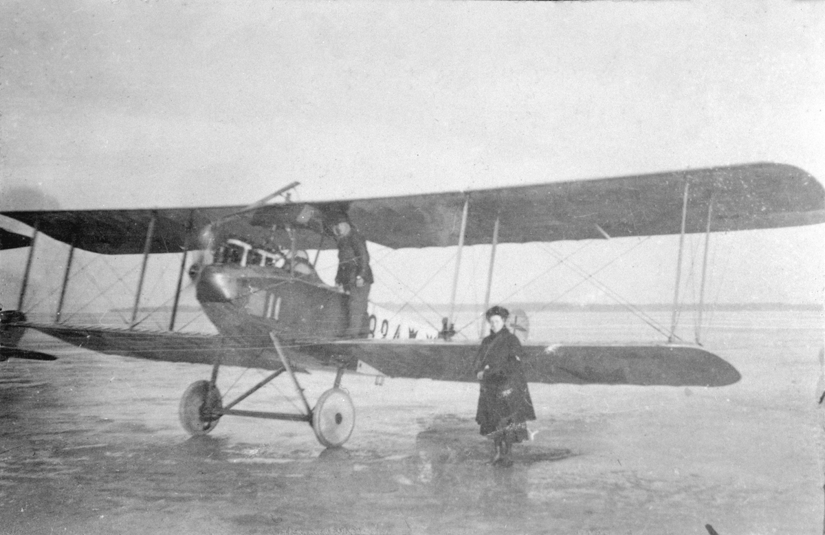 Flygplan Albatros nr 824 står på ett flygfält, vintertid. En mekaniker står på vingen och en civilklädd kvinna bredvid.