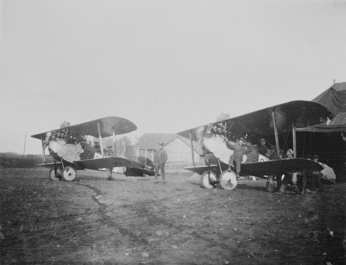 Två flygplan J 1, Phönix D. II motorkörs framför en tälthangar omkring 1920-1926. Militärer vid flygplanen.