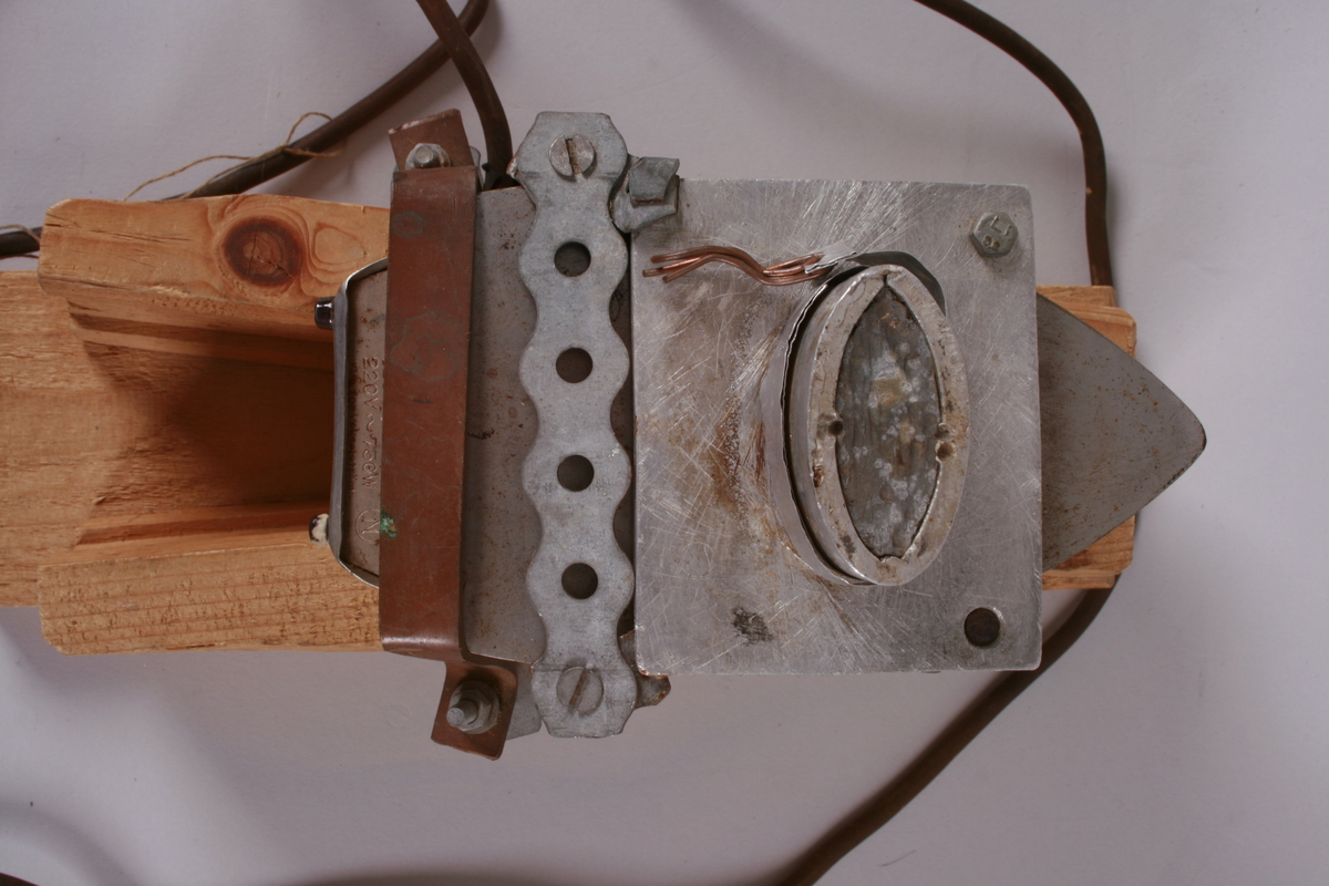 Strykejern med ledning og støpsel, montert opp ned i en treform. Medfølgende metallholder. Apparatet er trolig brukt til tilvirkning av sarg til fiolin.