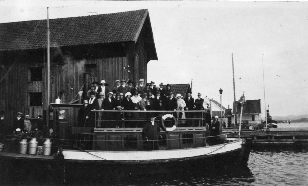Motiv med fergen "Stenviken" ved fergeleie i Langesund. Rutebåten tilhørte Wilhelm Nystrand og gikk i rute mellom Langesund og Skien. Her fullastet med folk og melkedunker ved Cudrios Sjøbod omkring 1920/30 tallet.