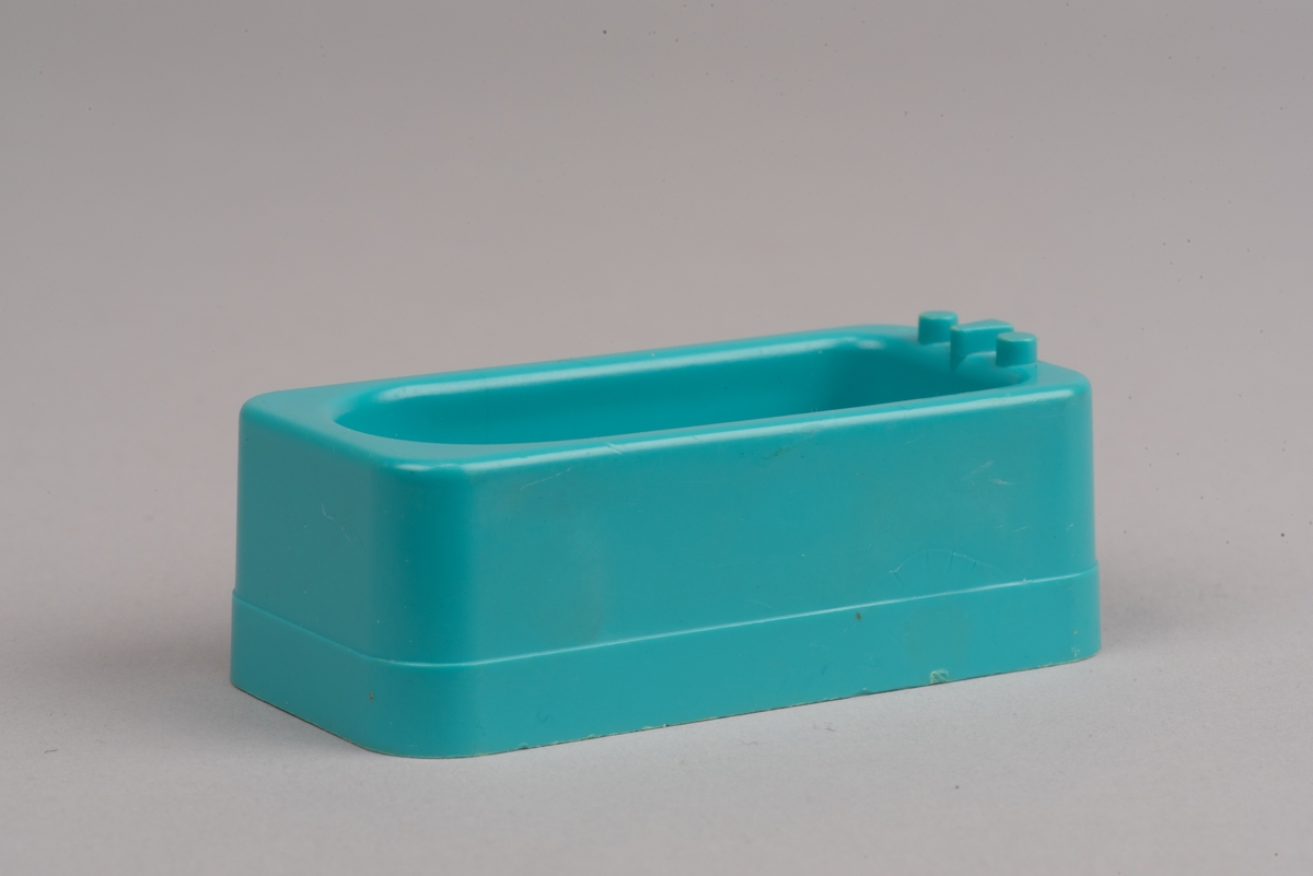 Dockskåpsmöbel i form av ett badkar tillverkat av plast.
Badkaret är rektangulärt i turkos färg. I botten finns ett avrinningshål och på den ena kortsidans övre kant sitter två kranar och en blandare, mycket förenklade i formen.