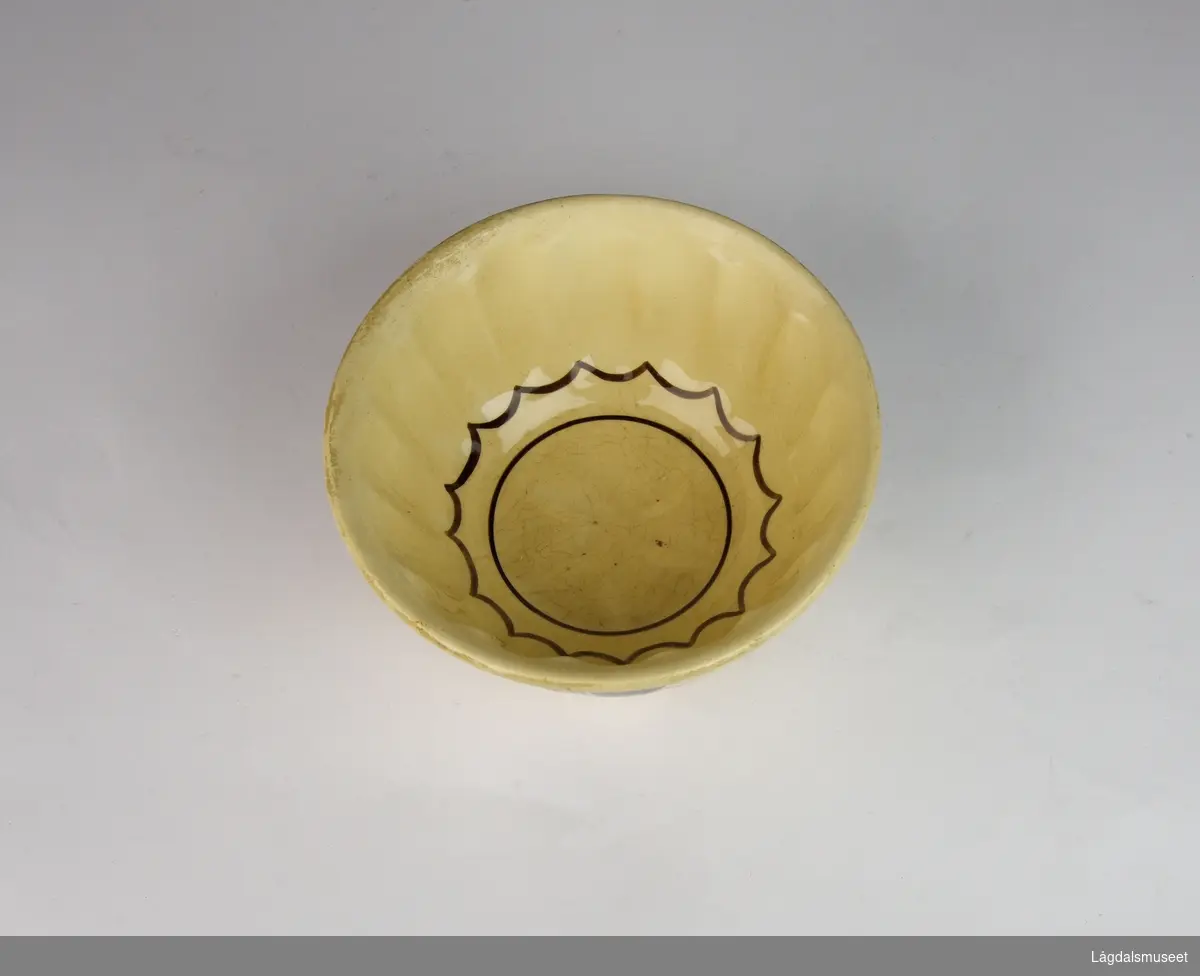 Enkel gulbrun husholdningsbolle med stilisert brun blomsterdekor på utsiden. På innsiden strekdekor.