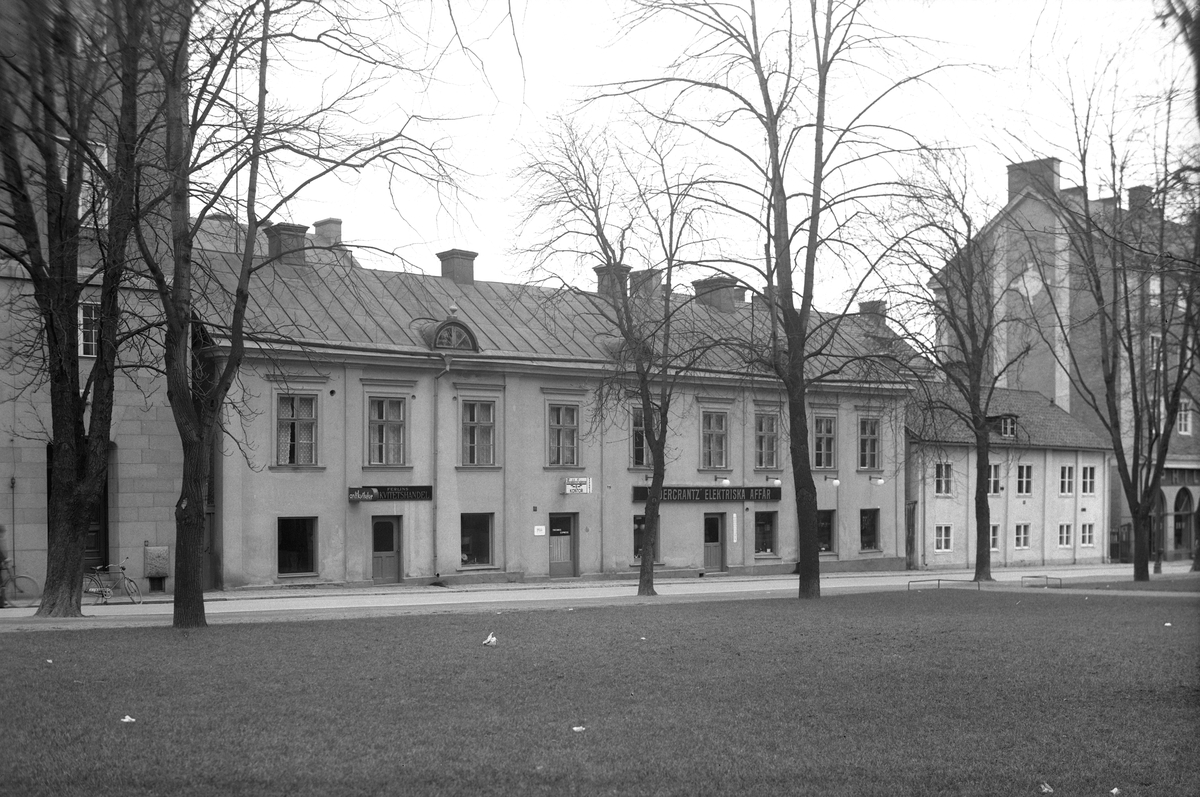 Parti av Ågatan i Linköping 1938. Vy från Sankt Larskyrkoparken mot den då kvarstående, äldre bebyggelsen i kvarteret Borgmästaren. Den långa byggnadskroppen närmast betraktaren hade innan det revs en lång och komplicerad byggnadshistoria, och torde sökt sitt ursprung i det sena 1700-talet. Genom en tids ägande av grevinnan Hedvig Cronhielm, född Boije, benämndes den Cronhielmska gården, men den som främst förknippats med gården är fröken Maria Sofia Westring, som från år 1833 disponerade densamma. I sitt testamente överlät hon vidare gården till Linköpings stad med syfte att brukas som så kallat arbetshus, en slags korrektionsanstalt, specifikt för kringstrykande bettlare. Stadens styrande ansåg månne fröken Westrings anspråk väl specificerade. Istället kom man i gården att inrymma stadens första, fasta brandkår. Det låga, ljusa gatuhuset längre ner vid gatan ingick i vad tiden kallade Dandenellska gården, där sista ägaren Emy Dandenelle ännu vid fotoåret bodde kvar.
