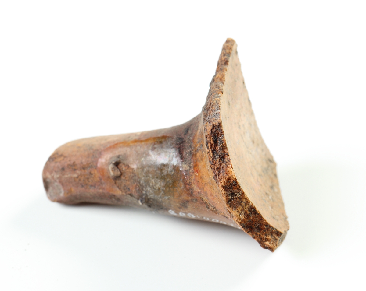 Koniskt ben samt del av kärlbuk i yngre rödgods, sannolikt från en trebensgryta. Brun glasyr på grytans insida, samt på delar av benet. Tillverkad i södra Skandinavien.