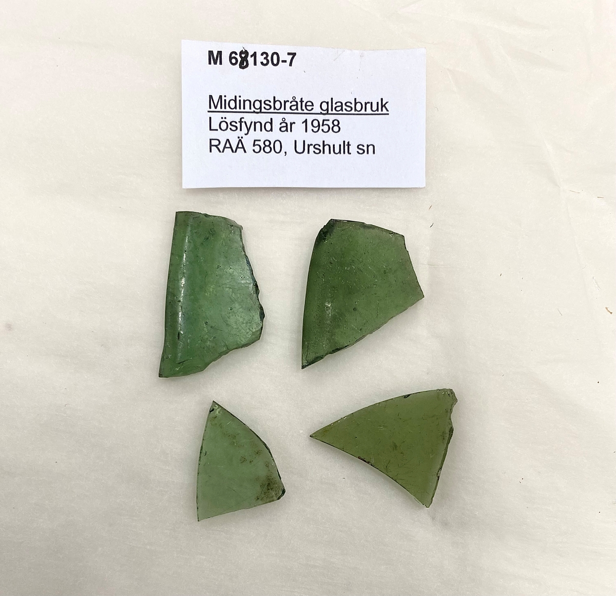 Fyra fragment av fönsterglas i grön glasmassa. Två av fragmenten har en mjukt rundad kant.