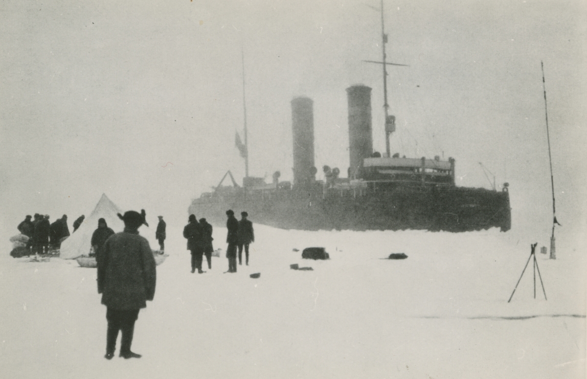 Fotografi från svenska undsättningsexpeditionen 1928. Motiv av den ryska isbrytaren Krasin, i förgrunden syns ett flertal expeditionsmedlemmar och ett tält.