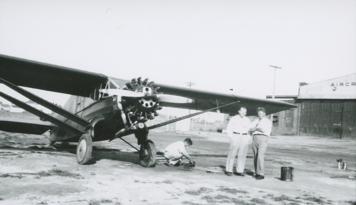 Fotografi från låda märkt Bernt Balchen. Balchen var norsk-amerikansk flygare, polarforskare och militär. Motiv av tre män som står på startbana vid ett flygplan. Mannen längst till höger är troligen Bernt Balchen.