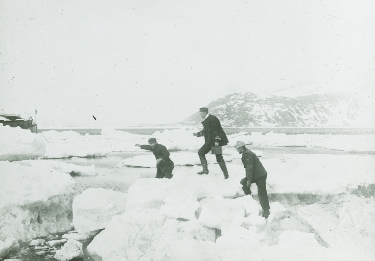 Glasnegativ med motiv av tre män som går på snöhögar invid vattnet. Till vänster skymtas ett fartyg i förgrunden.