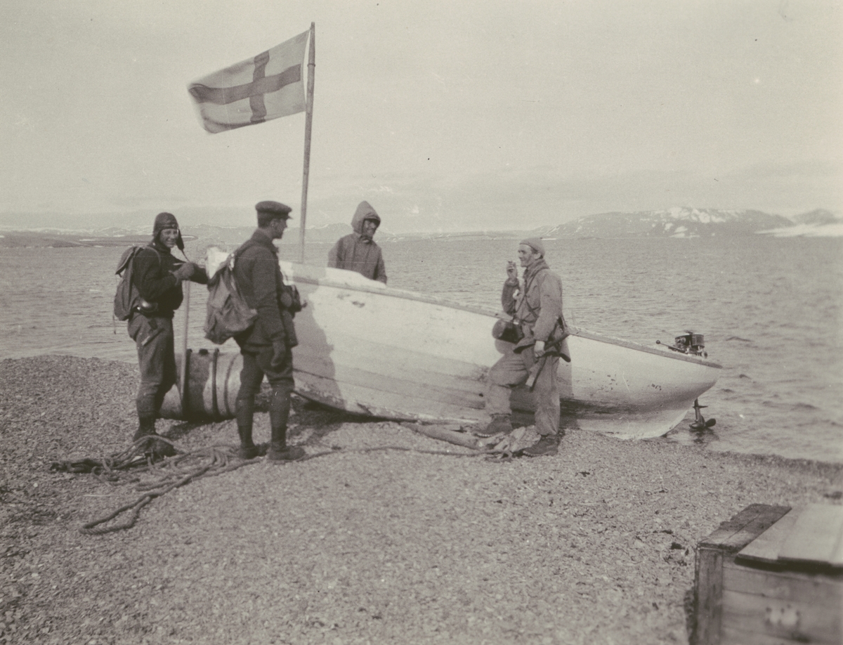 Fotografi från Ahlmannexpeditionen 1931. Motiv av fyra män vid båt på strand.