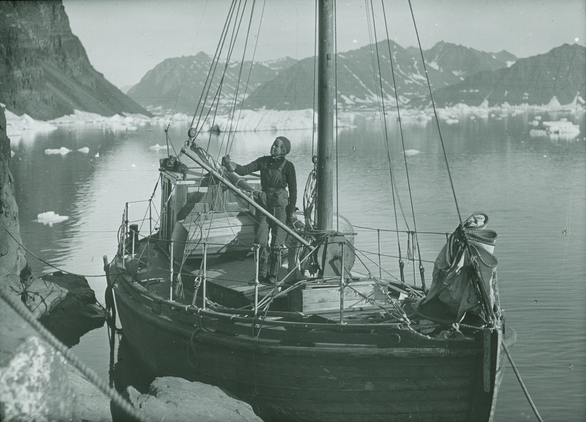 Fotografi från expedition till Spetsbergen. Motiv av kvinna ombord på båt med berg i bakgrunden.