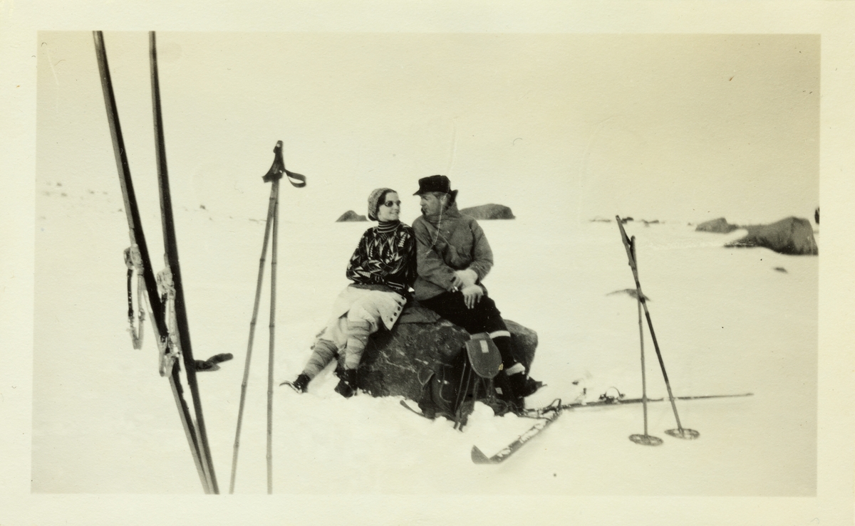 Et ungt par skigåere, antagelig Lucy Egeberg og Anton Fredrik Klaveness, hviler på en stein på Hardangerjøkulen. Fotografert påsken 1928.
