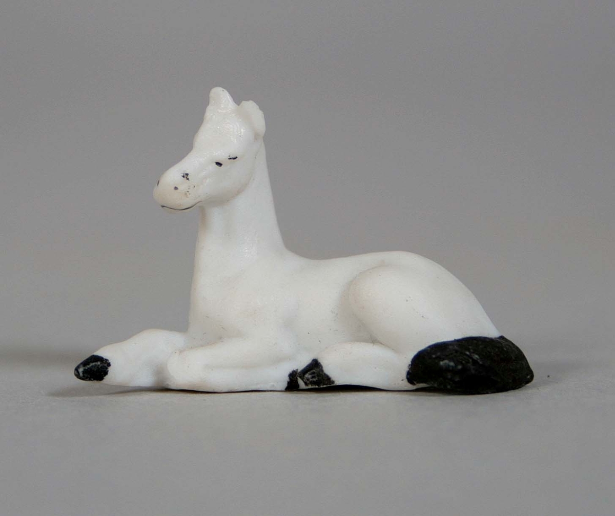 Liggande häst, i oglaserat vitt porslin med svartmålad svans och klövar.
