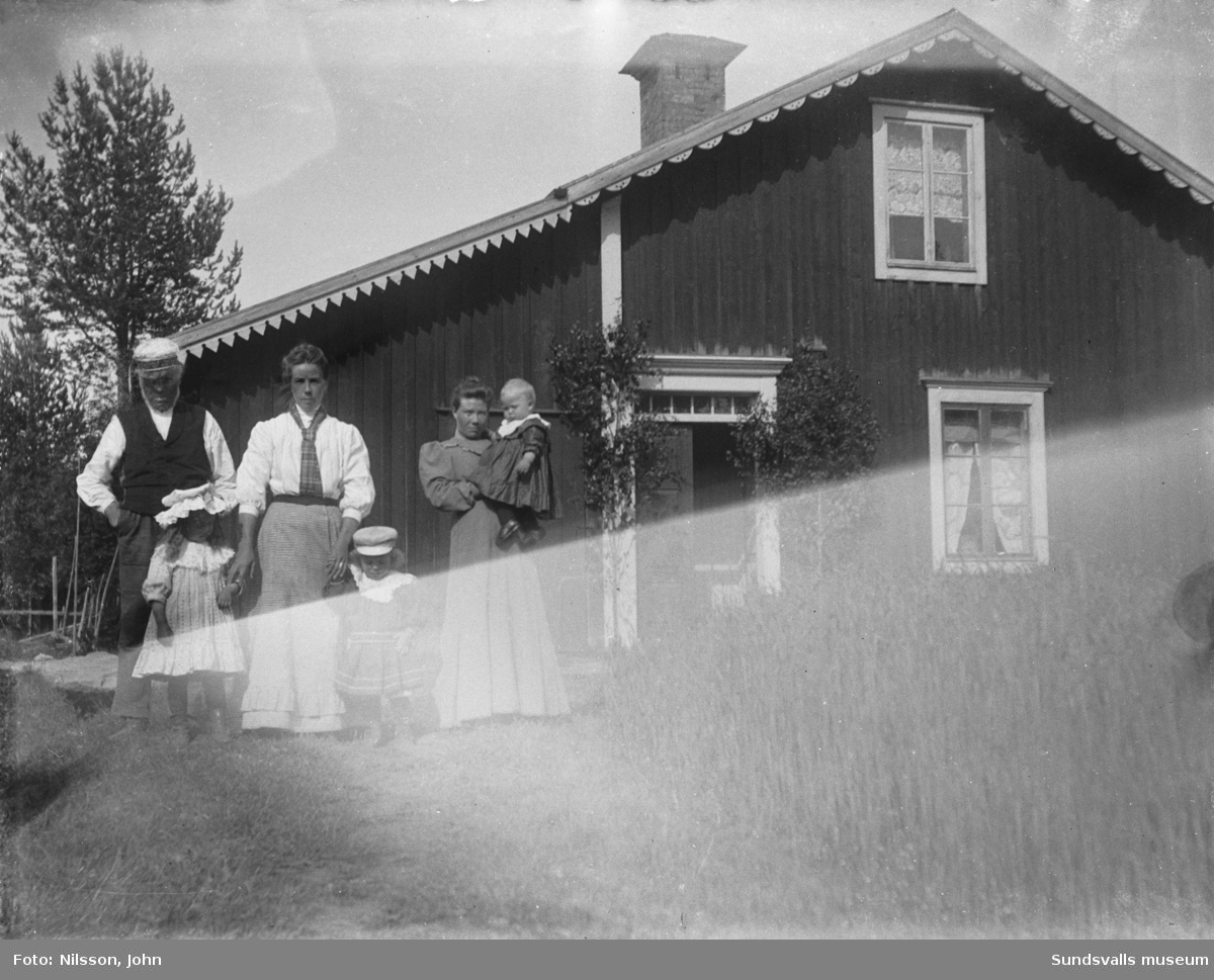 Familjeporträtt med två kvinnor och tre små barn framför en dubbeldörr med överljus. På bild nummer två från samma tillfälle finns även en äldre man med.