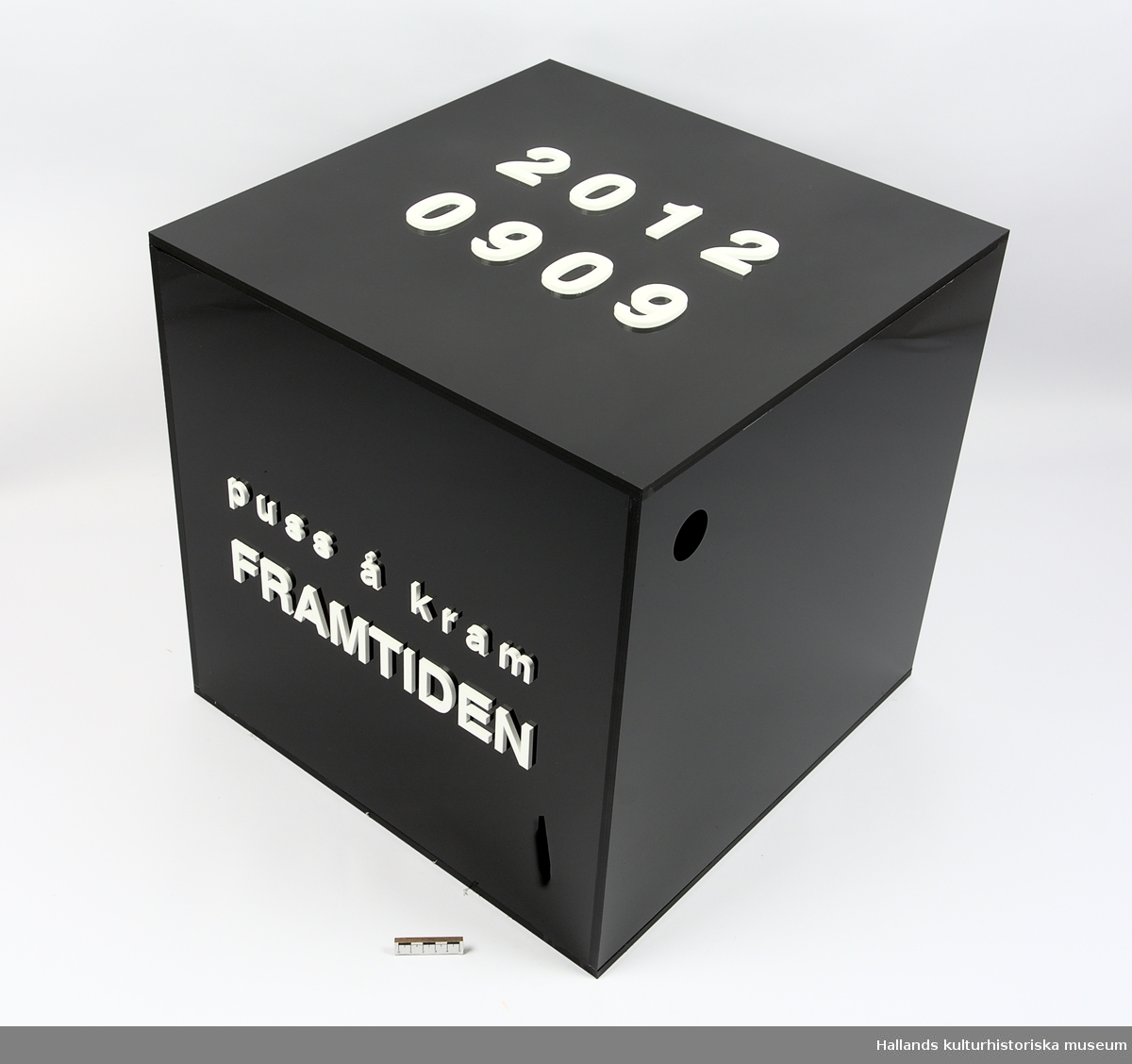 Konstinstallation i form av en kubformad låda av blankpolerad svart akrylplast. Lådan bär bokstäver av plast i högrelief på ovansidan samt på en av dess stående sidor. Text på ovansidan: "2012 0909". På den stående sidan: "puss å kram FRAMTIDEN". I hörnet på  en av de stående sidorna finns ett hål (40 mm diameter), men lådan är i övrigt helt försluten och saknar lock.

Innehållet är okänt.