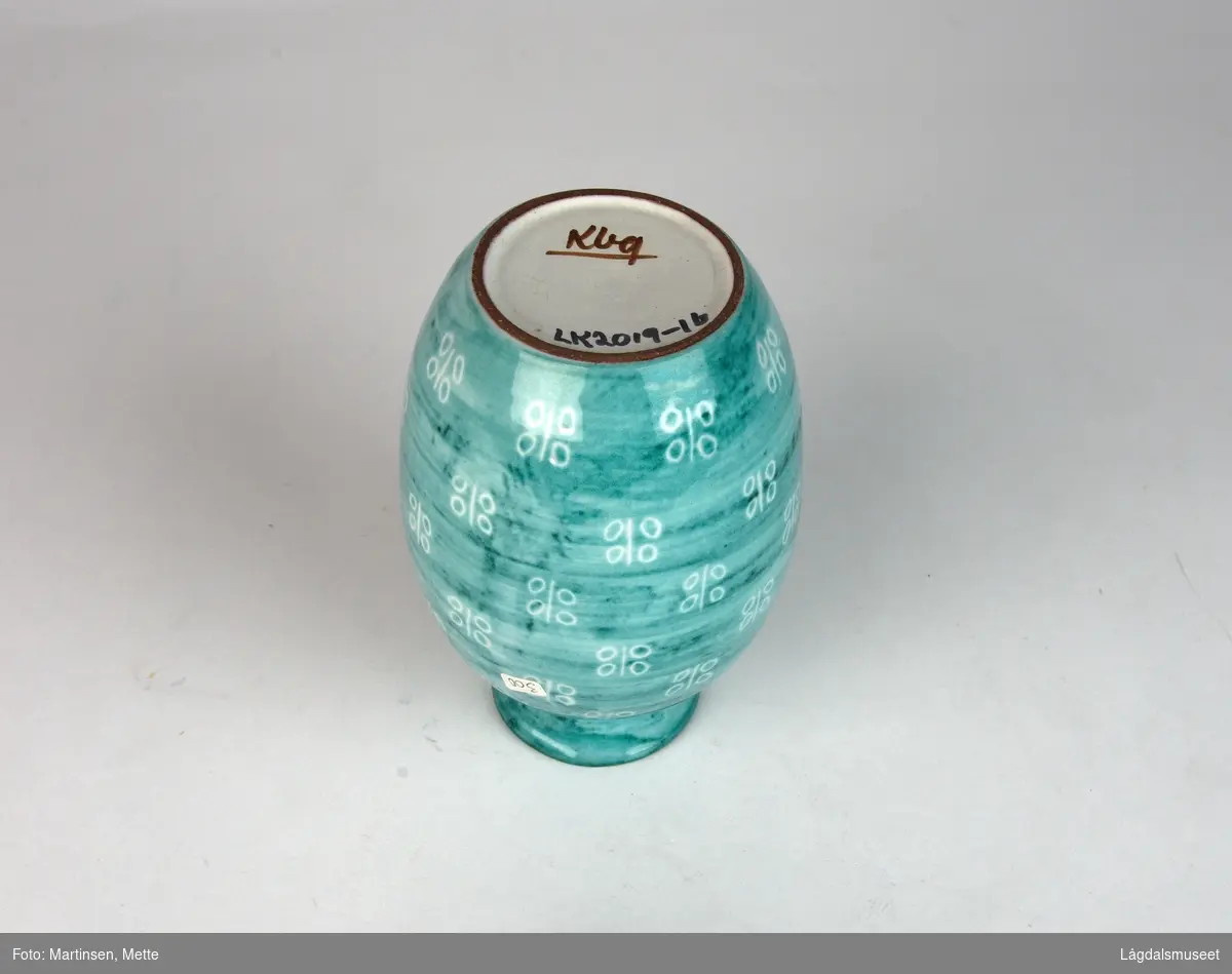 Dreid vase med grønn og hvit glasur. I sju høyder går det rundt vasen linjer med stiliserte blomster eller en plante med blad.