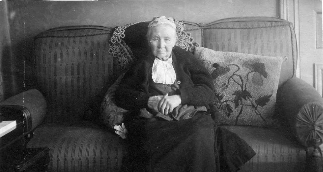 En äldre kvinnan sitter i en tresits-soffa.