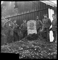 Soldater er samlet rundt en lav bautastein, antageligvis i o