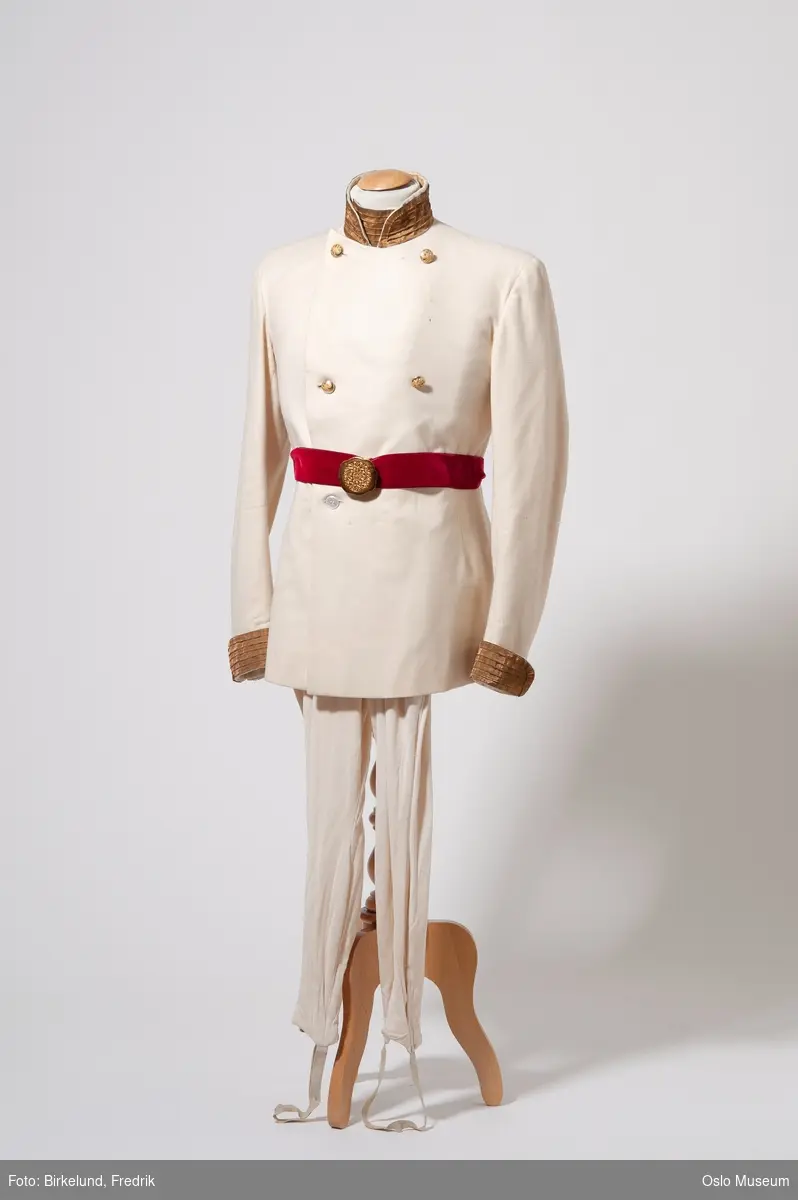 A: uniformsjakke, hvit ull med gull på oppstående krave og rundt ermekant
B: lange, hvite silkebukser fra Silkehuset
C: belte i rød fløyel med gullspenne
D: belte (?) i grønn fløyel