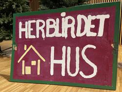 Et håndmalt skilt påført "Her blir det hus" og en enkel tegning av et hus
