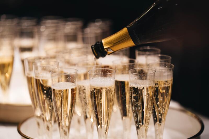 Mange stettglass på rad og rekke fylt med boblende champagne. En vinflaske skjenker fra høyre. Fotografi.